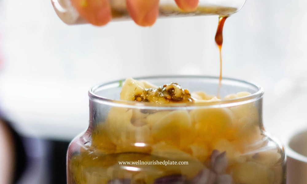 Pouring a mustard dressing over a tuna pasta salad in a jar