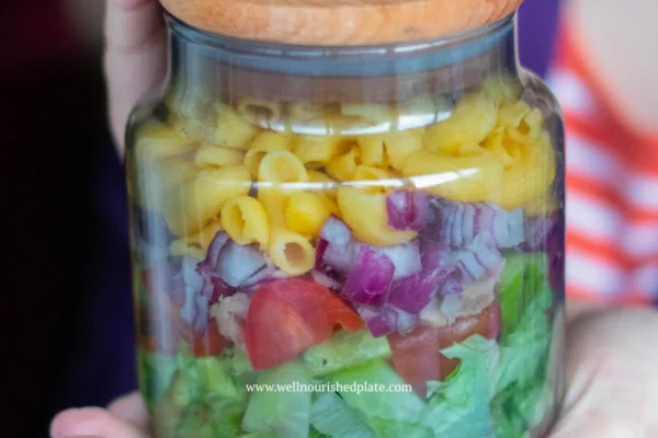 woman holding a gluten free pasta salad in a jar